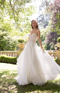 Ein zartes aber dennoch verführerisches A- Linien Hochzeitskleid aus Chiffon. Das Kleid hat einen trägerlosen herzförmigen Ausschnitt. Das gesamte Oberteil des Brautkleides ist mit Spitzenapplikationen verziert. Ein Hingucker des Kleides ist der geraffte Rock mit den fließenden unterschiedlichen wellenartigen Chiffonlagen, die sich auch in der Schleppe wiederfinden. Das Brautkleid lässt sich durch eine Schnürung im Rückenbereich schließen. Optional ist das Kleid auch mit einem Reißverschluss und Kristallknöpfen erhältlich. 