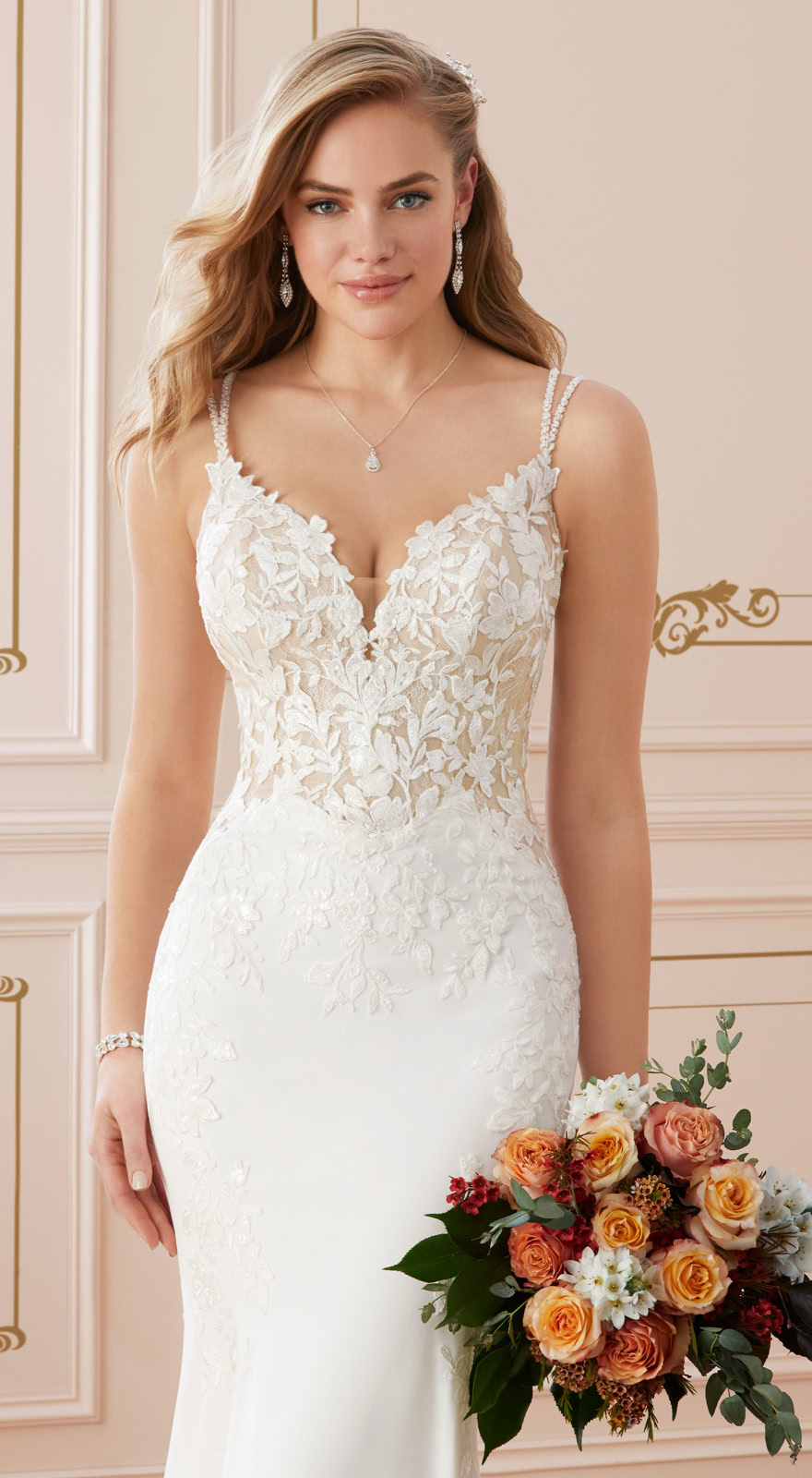 Frau in einem weißen Brautkleid mit Spitzenoberteil, hält einen Blumenstrauß mit orangefarbenen und weißen Blumen.