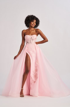 Eine Person in einem rosa, schulterfreien Kleid mit hohem Schlitz, stehend vor einem neutralen Hintergrund.