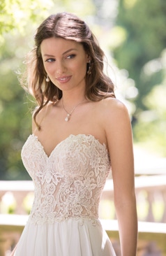 Ein zartes aber dennoch verführerisches A- Linien Hochzeitskleid aus Chiffon. Das Kleid hat einen trägerlosen herzförmigen Ausschnitt. Das gesamte Oberteil des Brautkleides ist mit Spitzenapplikationen verziert. Ein Hingucker des Kleides ist der geraffte Rock mit den fließenden unterschiedlichen wellenartigen Chiffonlagen, die sich auch in der Schleppe wiederfinden. Das Brautkleid lässt sich durch eine Schnürung im Rückenbereich schließen. Optional ist das Kleid auch mit einem Reißverschluss und Kristallknöpfen erhältlich. 