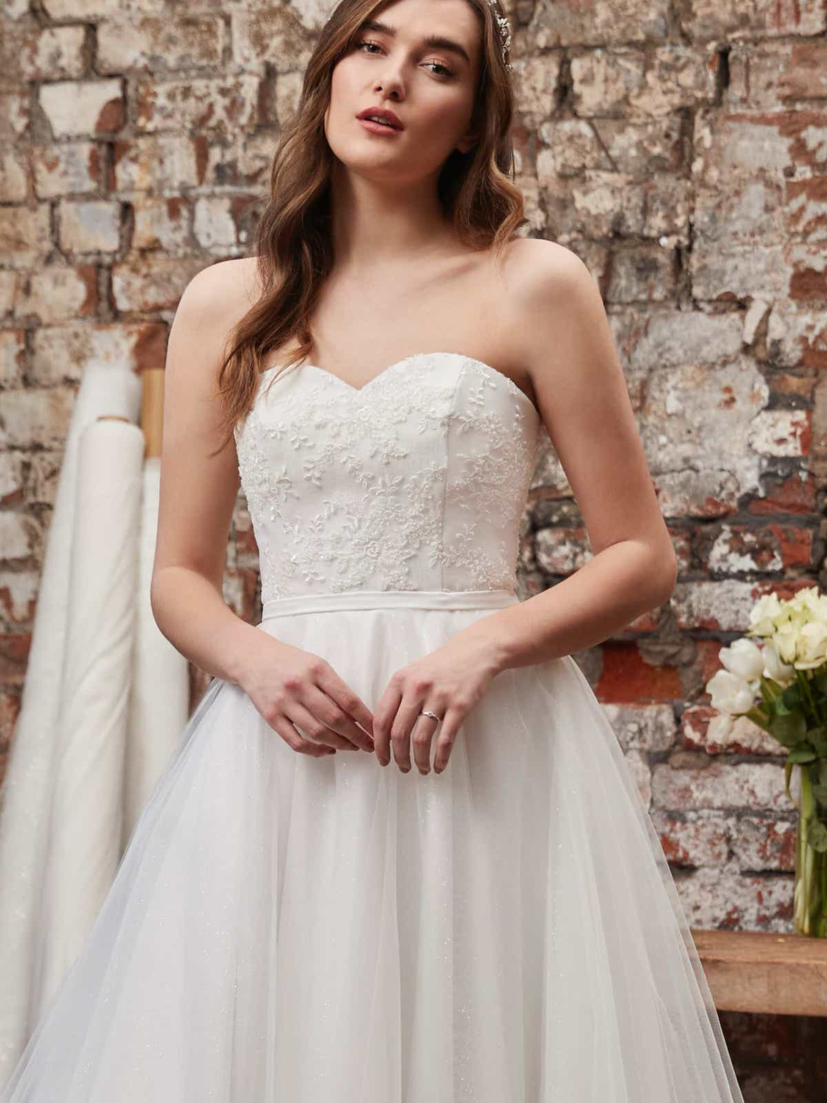 51013 Ein wundervolles romantisches Brautkleid. Ein bezaubernder Herzausschnitt, ein funkelnder Softtüll-Rock, moderne Spitzenapplikationen und ein figurbetonter Taillengürtel umrahmen die A-Linie. Geschlossen wird das Brautkleid mithilfe eines Reißverschlusses im Bereich des Rückens. 