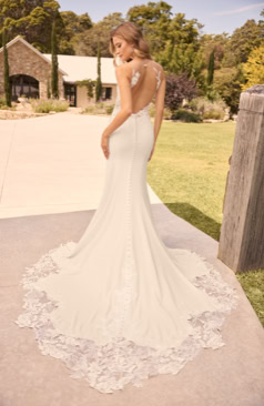 Modernes Brautkleid FM52137 aus edlem Crêpe mit transparenter Rückenpartie, Knopfleiste und floraler Spitzenschleppe. Erhältlich bei FM Braut- und Abendmode in Sandkrug bei Oldenburg.